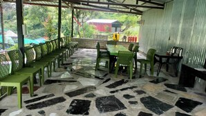 A covered outdoor seating area with stone flooring and green chairs. - Phulwari Resort (Ukhimath)