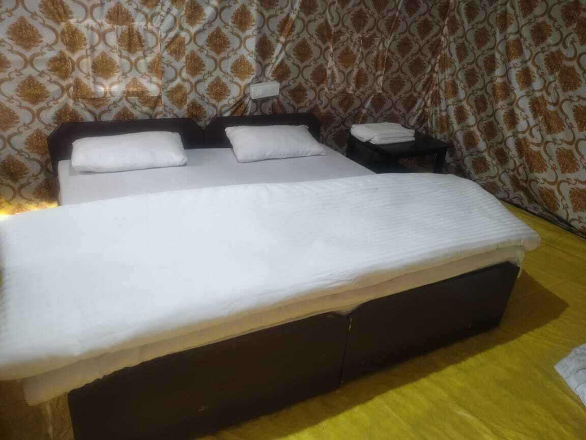 Un lit avec une literie blanche et une tête de lit sombre, une table de chevet avec une lampe et un papier peint à motifs.