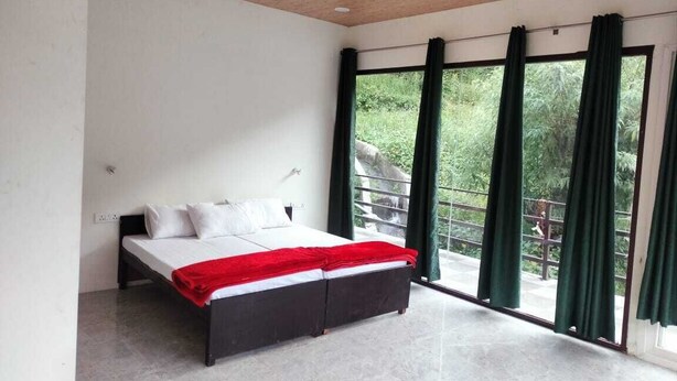 A modern bedroom with a large bed, a wooden ceiling, and a balcony with green curtains. - Phulwari Resort (Ukhimath)