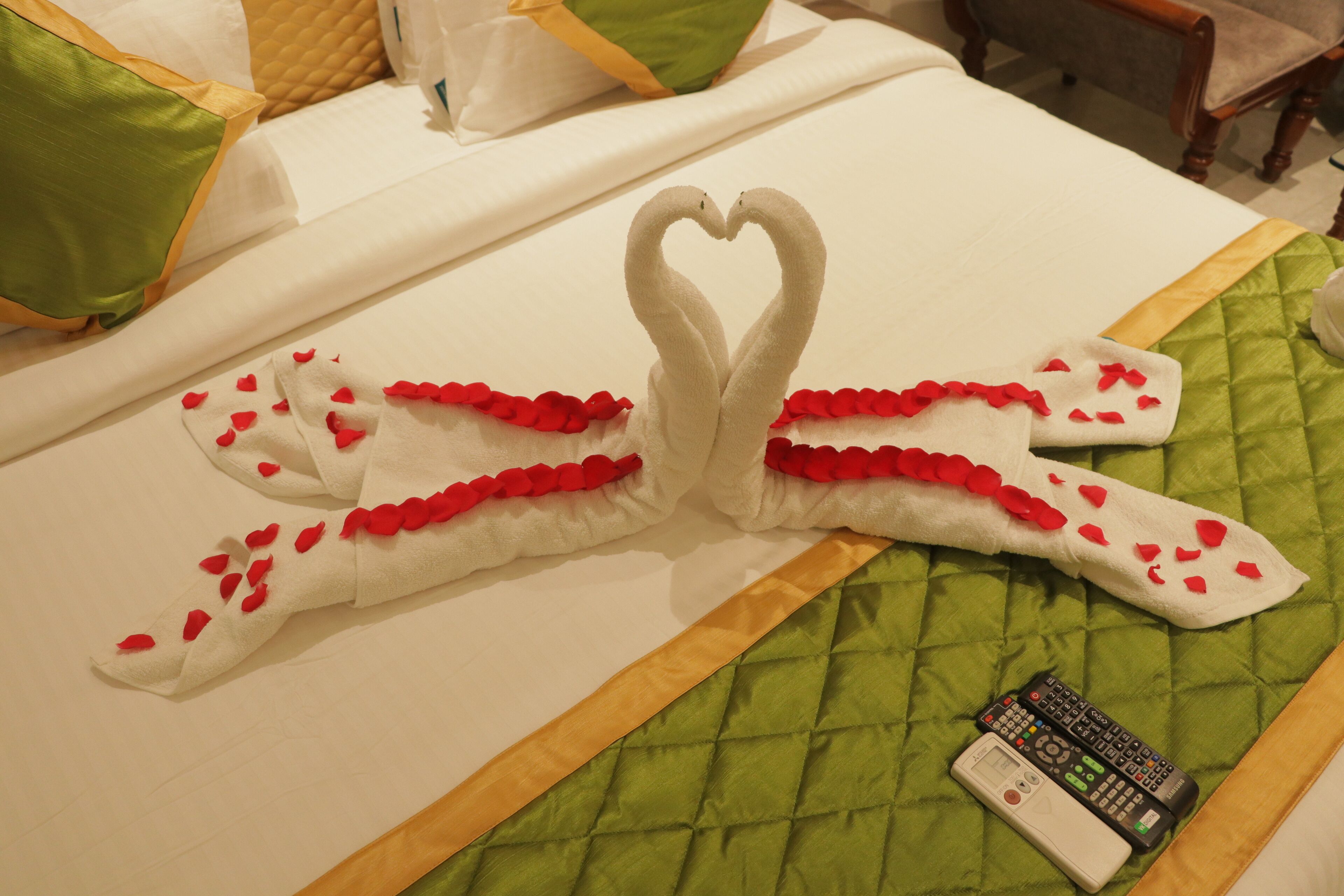 A bed with a heart-shaped towel decoration and a remote control on the bed.
