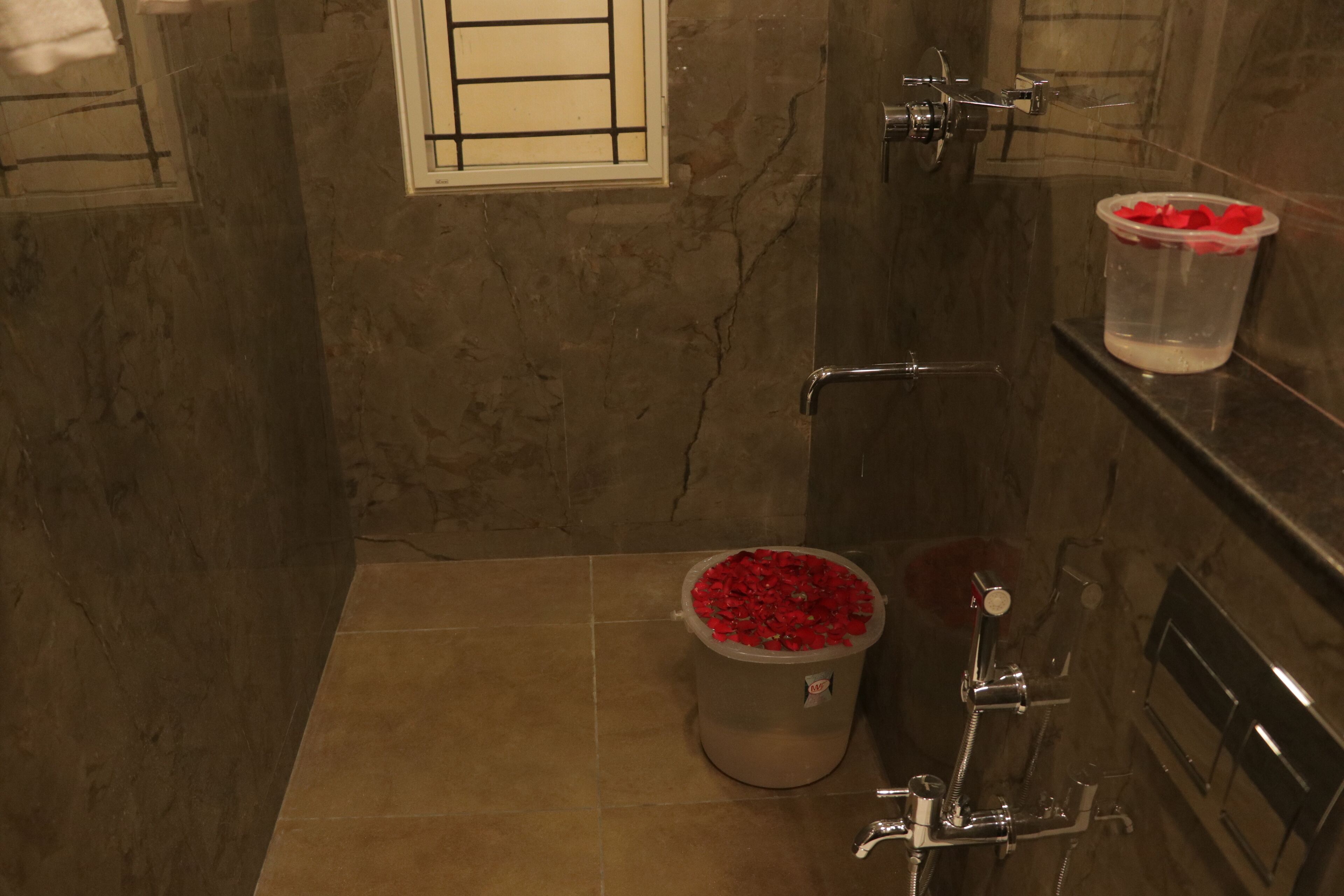 A bathroom with a marble wall, a shower, and a toilet with a trash bin.