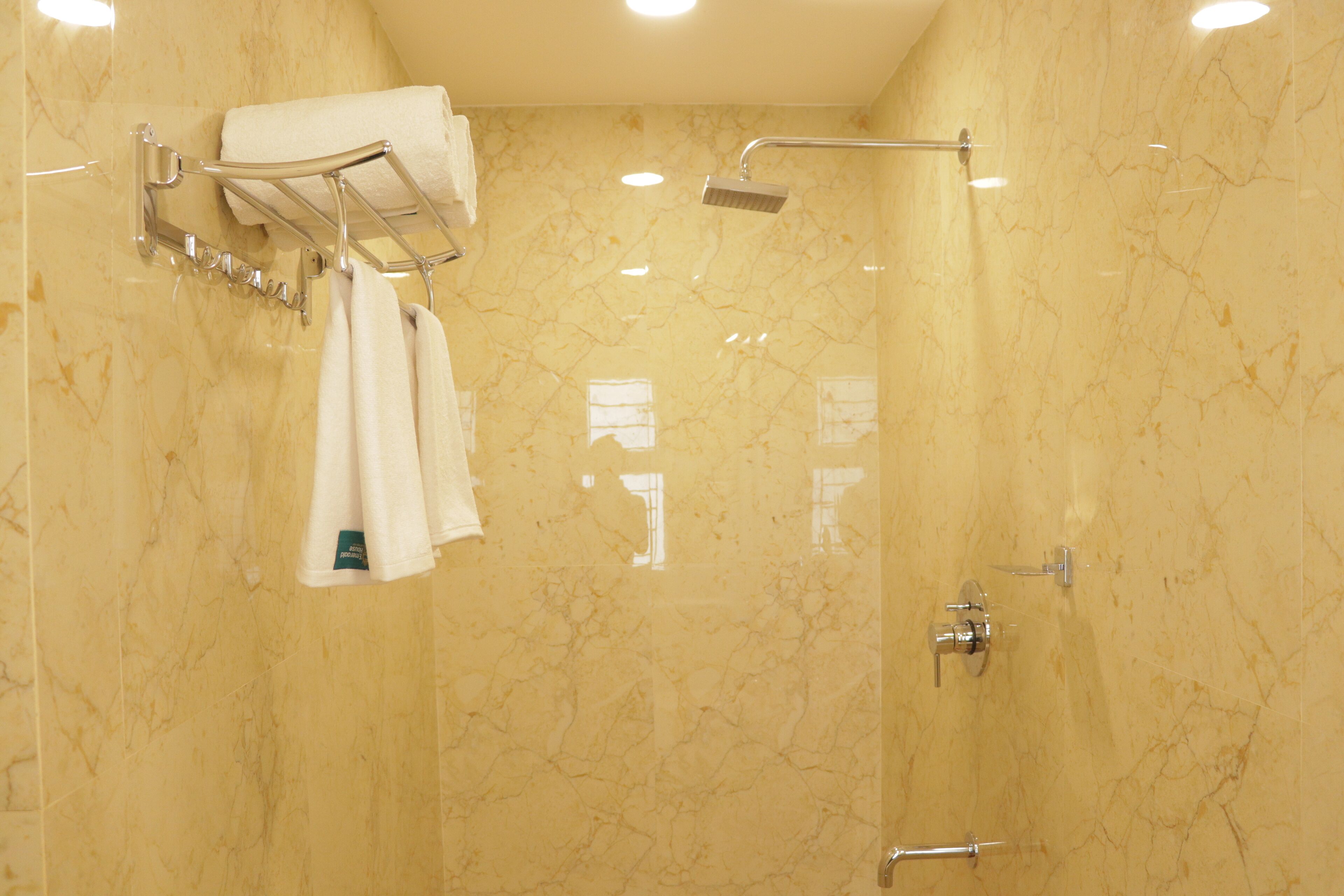 A bathroom with a marble wall, a towel rack with two towels, a handheld showerhead, and a wall-mounted faucet.