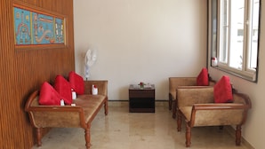 Une pièce comprenant deux canapés en bois avec des coussins rouges, une petite table avec un vase et un ventilateur fixé au mur.