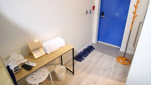 Habitació petita amb escriptori de fusta, una cadira, una porta blava i un penjador amb sabates.
