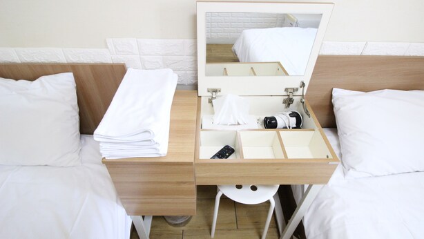 Habitació d'hotel amb dos llits, una nitròria de fusta amb mirall i un tamboret petit de color blanc.