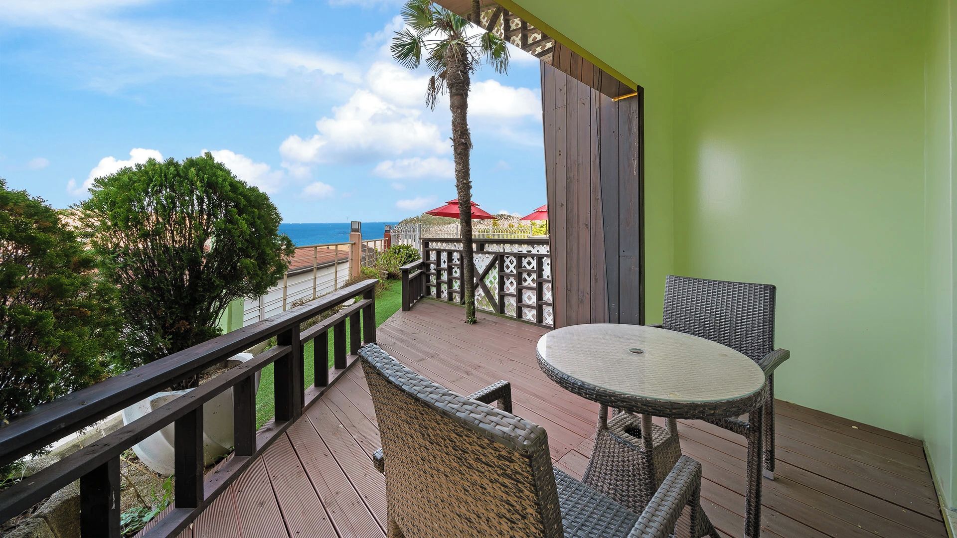 A wooden deck with wicker furniture, a view of the ocean, and a green wall.