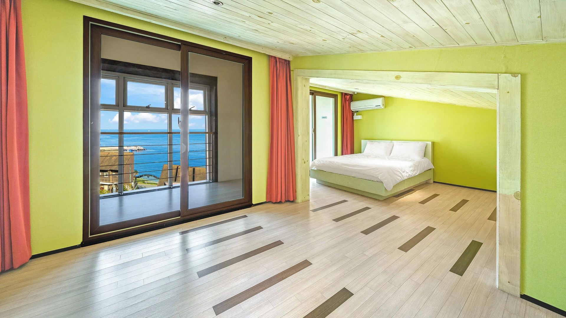 A hotel room with a large sliding glass door leading to a balcony with a view of the sea.