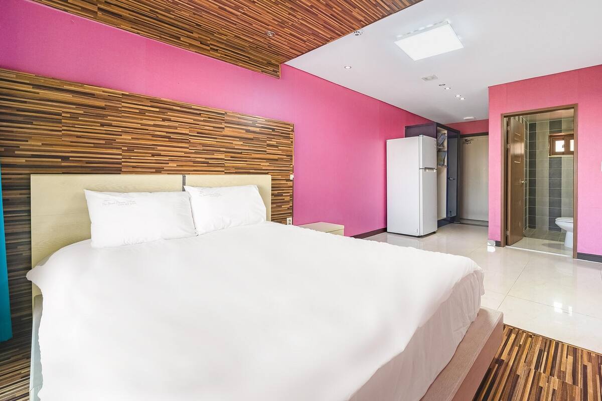 A modern hotel room with a large bed, a wooden headboard, and pink walls.