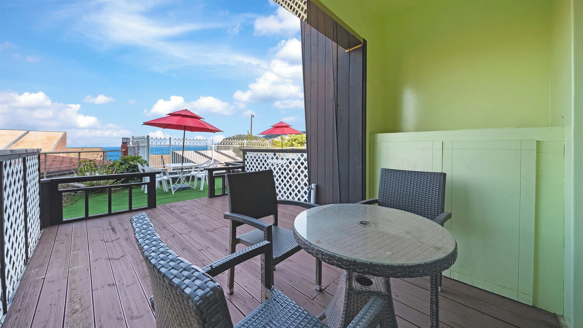 A covered outdoor seating area with wicker furniture, a round table, and red umbrellas.