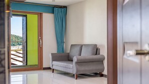 Ein Zimmer mit einem grauen Sofa, einer Schiebetür zum Balkon und einem türkisfarbenen Vorhang.
