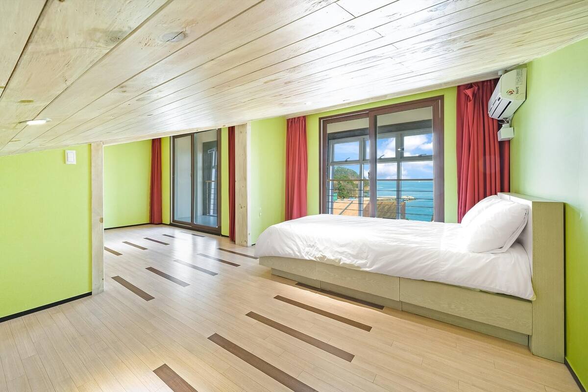 A room with a bed, a window with a view, and a wooden floor.