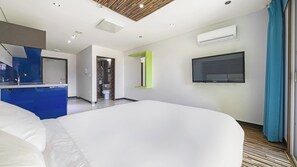 Une chambre d’hôtel moderne, dotée d’un grand lit, d’une télévision, d’un système de climatisation et d’une salle de bain visible à travers une porte ouverte.