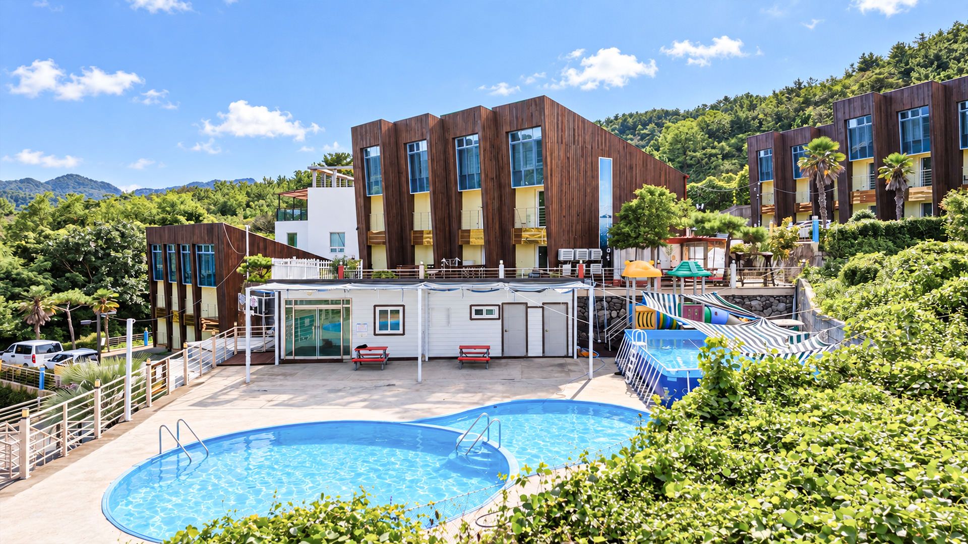A resort with two swimming pools, a covered area with seating, and a building with multiple windows.