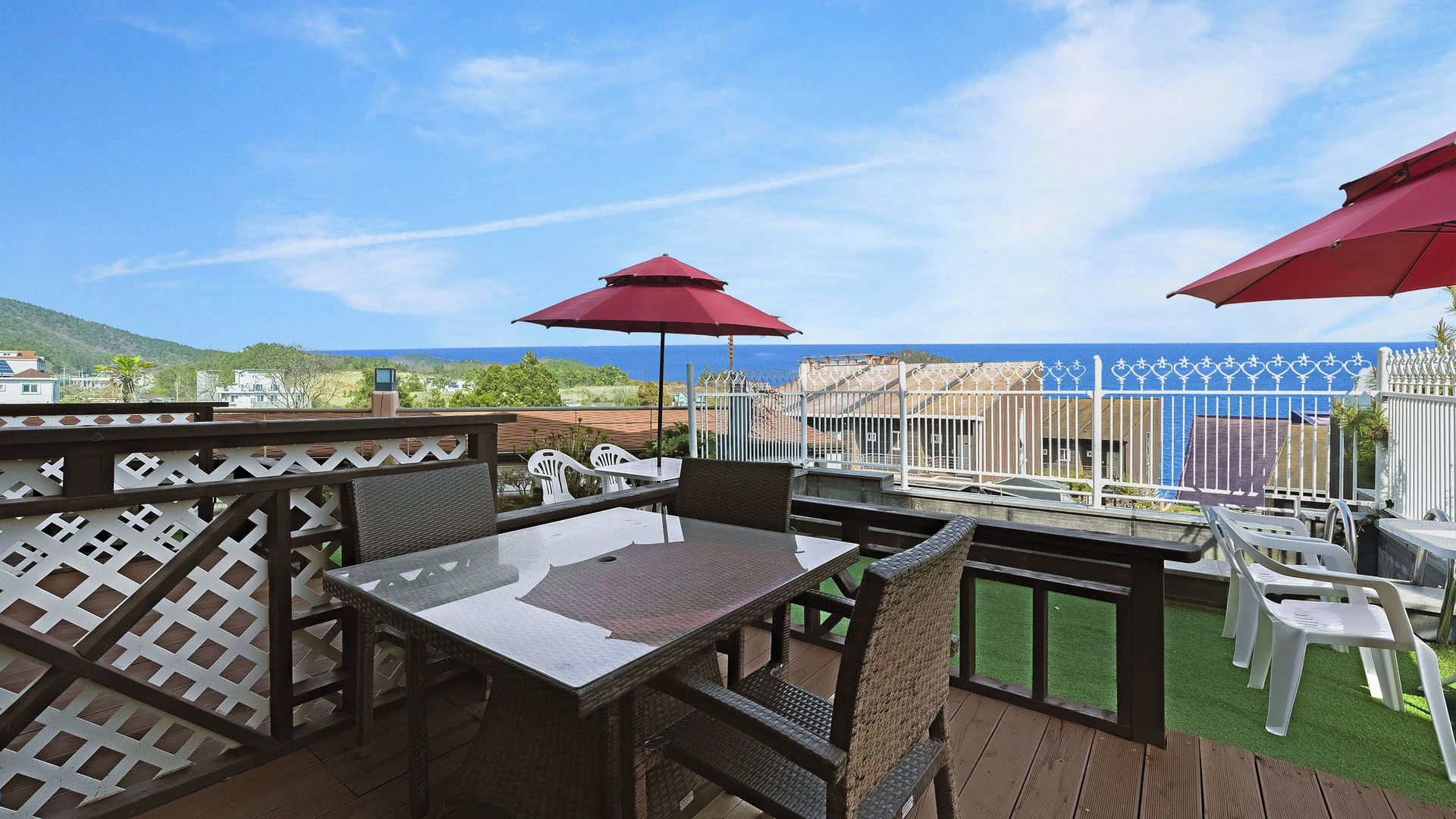 An outdoor patio with a table and chairs, a red umbrella, and a view of the sea.