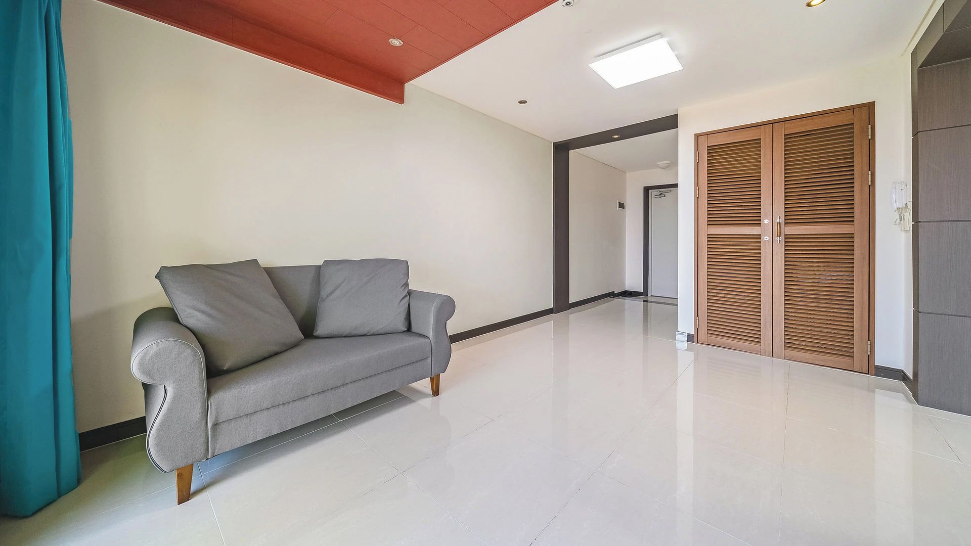 Un salon moderne avec un canapé gris, un plancher en bois et une porte en bois dotée de panneaux à persiennes.