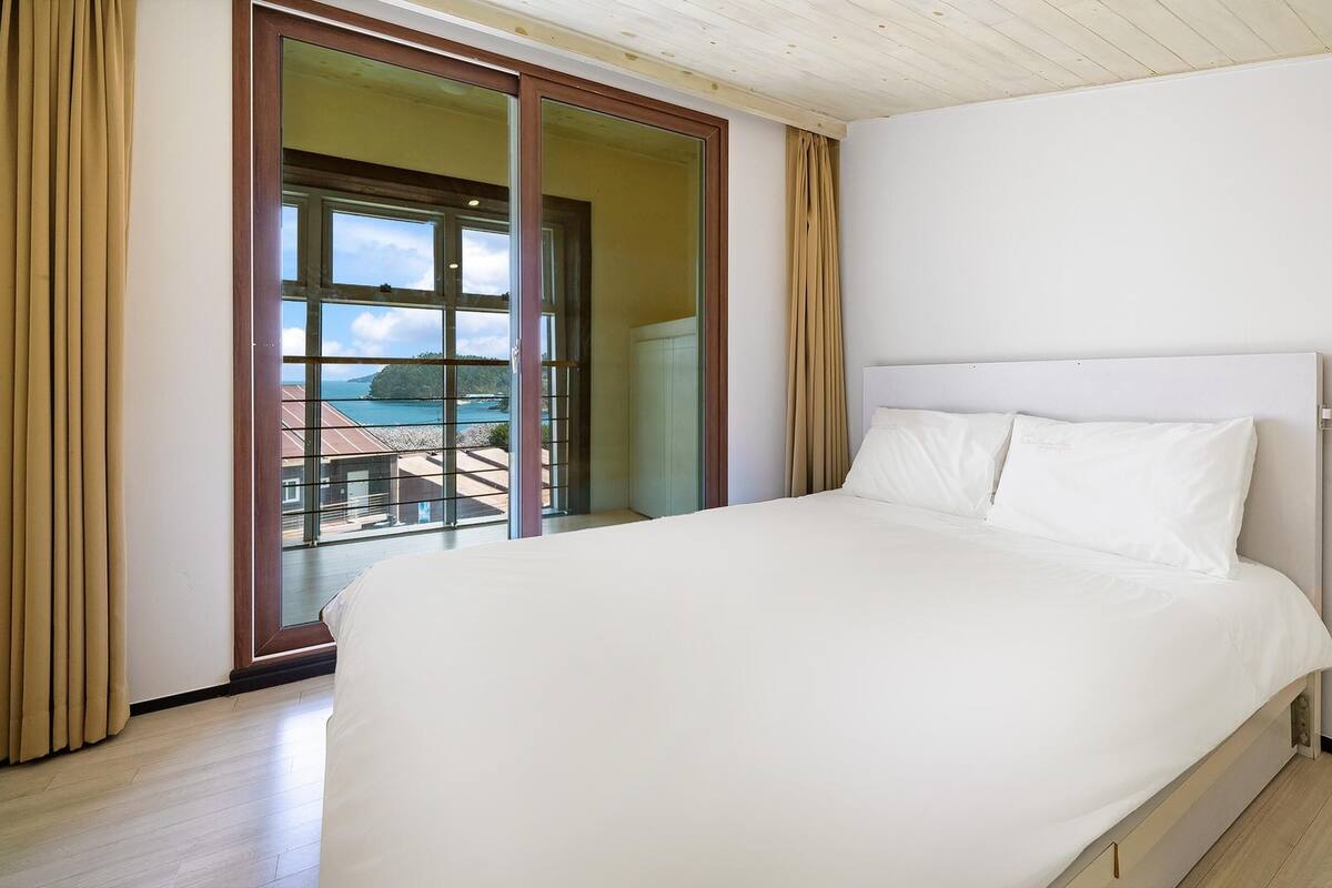 A bedroom with a large bed, a sliding glass door leading to a balcony, and a view of the sea.