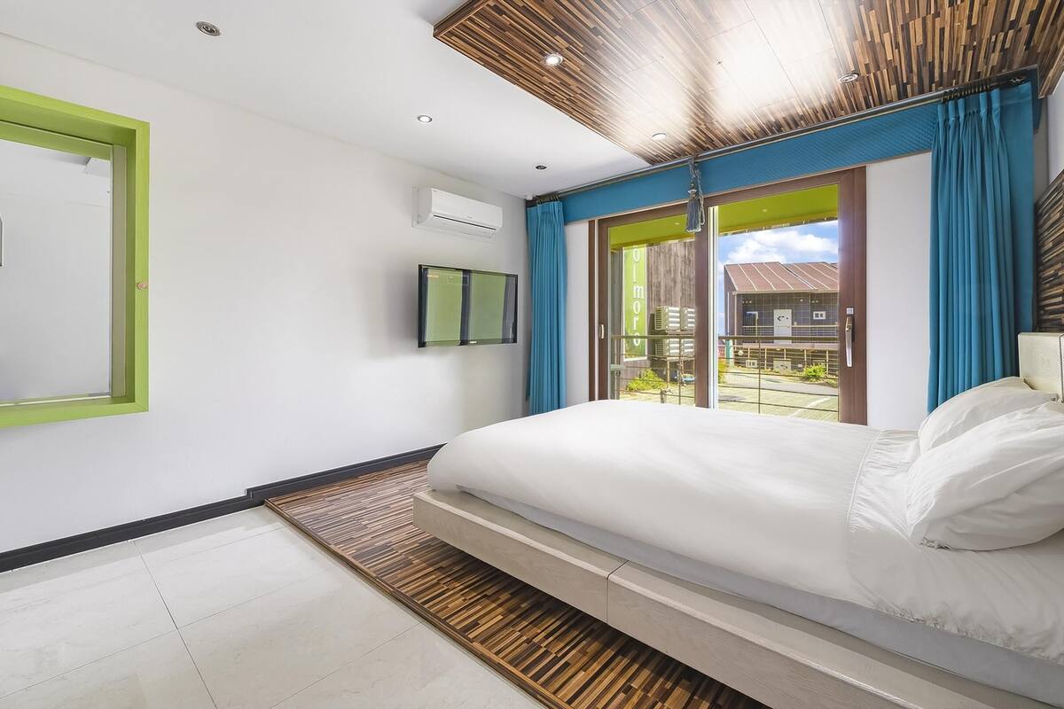 A modern bedroom with a large bed, a mirror, and a view of the outside.