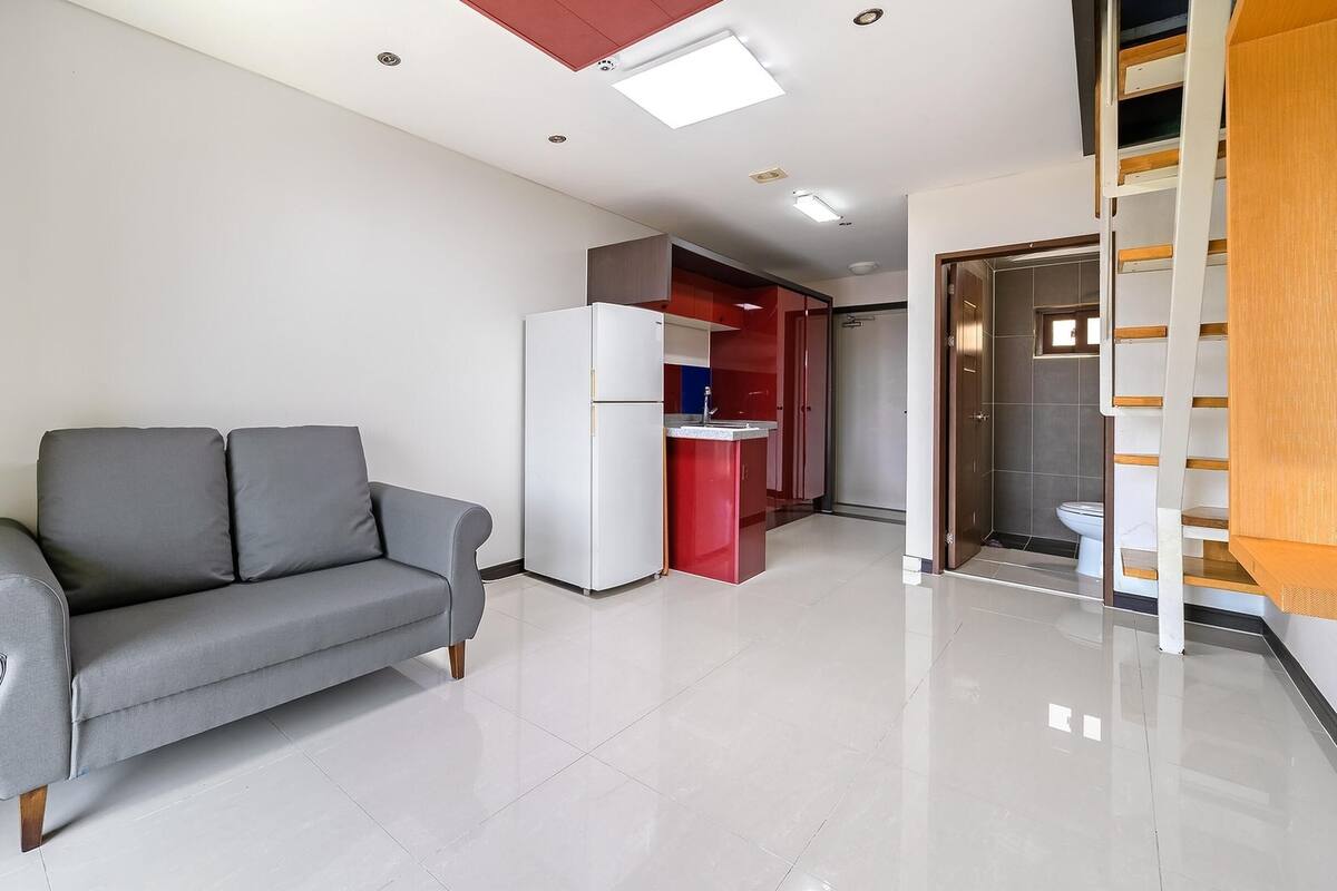 A modern living room with a grey sofa, a white refrigerator, and a red kitchen cabinet.