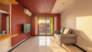 A modern hotel room with a flat-screen TV mounted on the wall, a sofa, and a sliding glass door leading to a balcony with a view of a mountain. - Geojedo Pilos Ocean View Pension (Geoje)