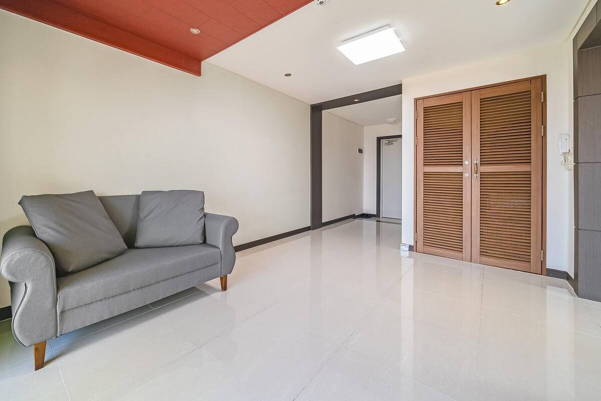 A modern living room with a grey sofa, wooden floor, and a wooden door with louvered panels.