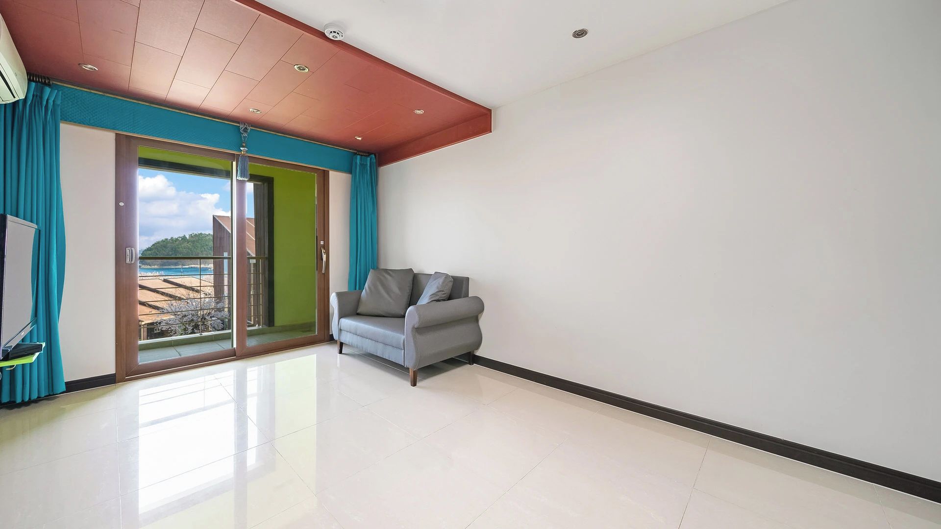 A spacious room with a sliding glass door leading to a balcony with a view of the beach.