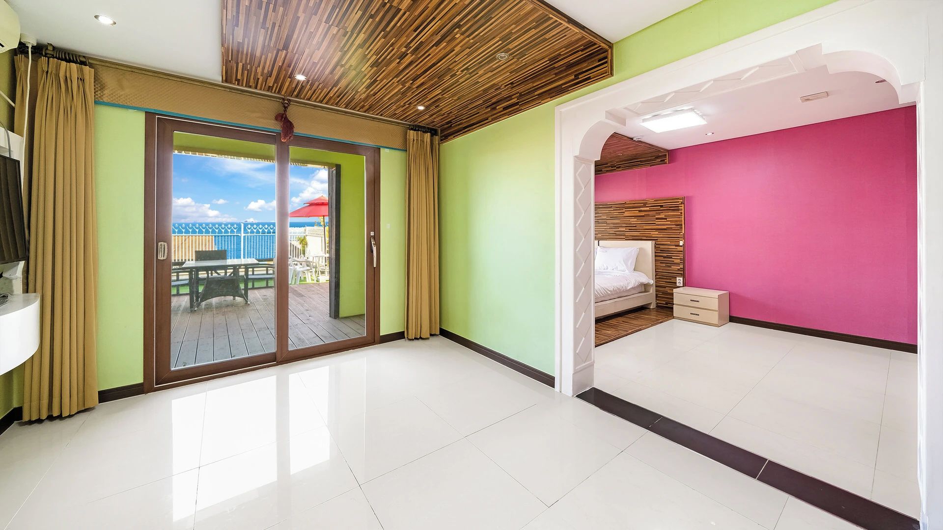 A room with a sliding glass door leading to an outdoor deck, a bed with a wooden headboard, and a bright pink accent wall.