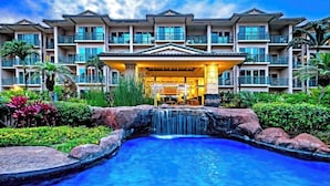 A hotel with a pool, a waterfall, and a well-maintained garden.