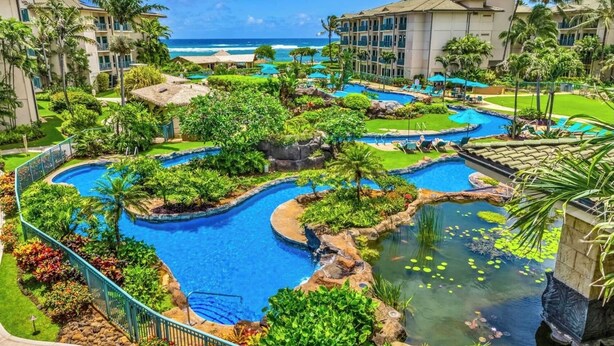 A resort with multiple swimming pools surrounded by lush greenery and palm trees, overlooking a beach.