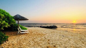A beach with a thatched umbrella and lounge chairs.