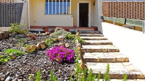 Ein Haus mit Ziegeldach, einer Haustür und einem kleinen Garten mit Steinen und Blumen.