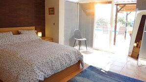 Ein Schlafzimmer mit einem Bett, einem Sessel und Blick ins Freie.