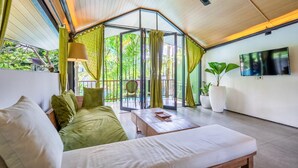 Una habitación con cama, sofá, mesa de centro, televisión y ventanas grandes con cortinas.