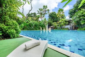 A swimming pool with a tiled edge, surrounded by lush greenery and a clear sky.