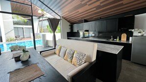A modern kitchen with dark cabinets, a large island, and a dining area with a sofa and table. - Exclusive Villa F3 with Jacuzzi - MANA VILLAS (Benoa)