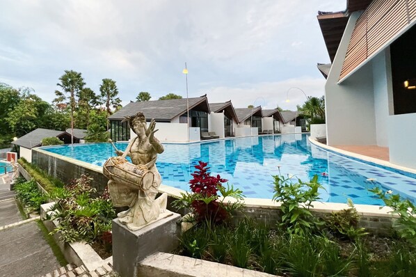 A swimming pool with a statue, surrounded by greenery and modern buildings.