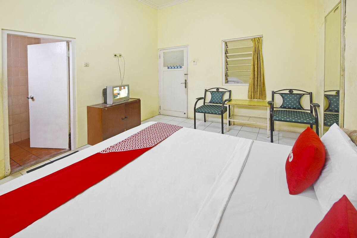 Une chambre d’hôtel avec un lit, deux chaises, un bureau, une télévision et une porte.
