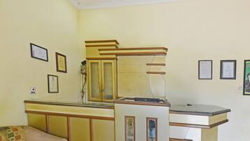 A room with a beige wall, a wooden cabinet with glass doors, a small sofa, and framed certificates on the wall.