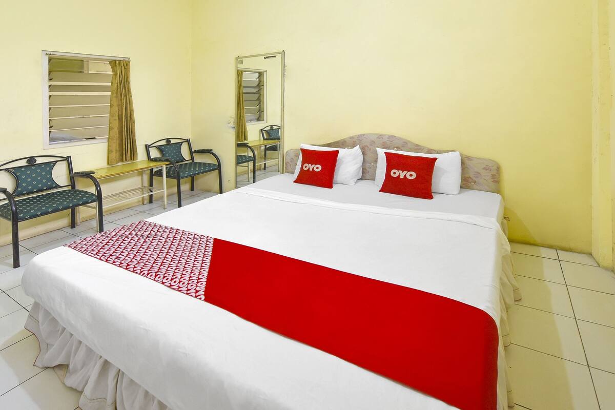 Une chambre d’hôtel avec un lit, deux chaises, une petite table et un miroir.