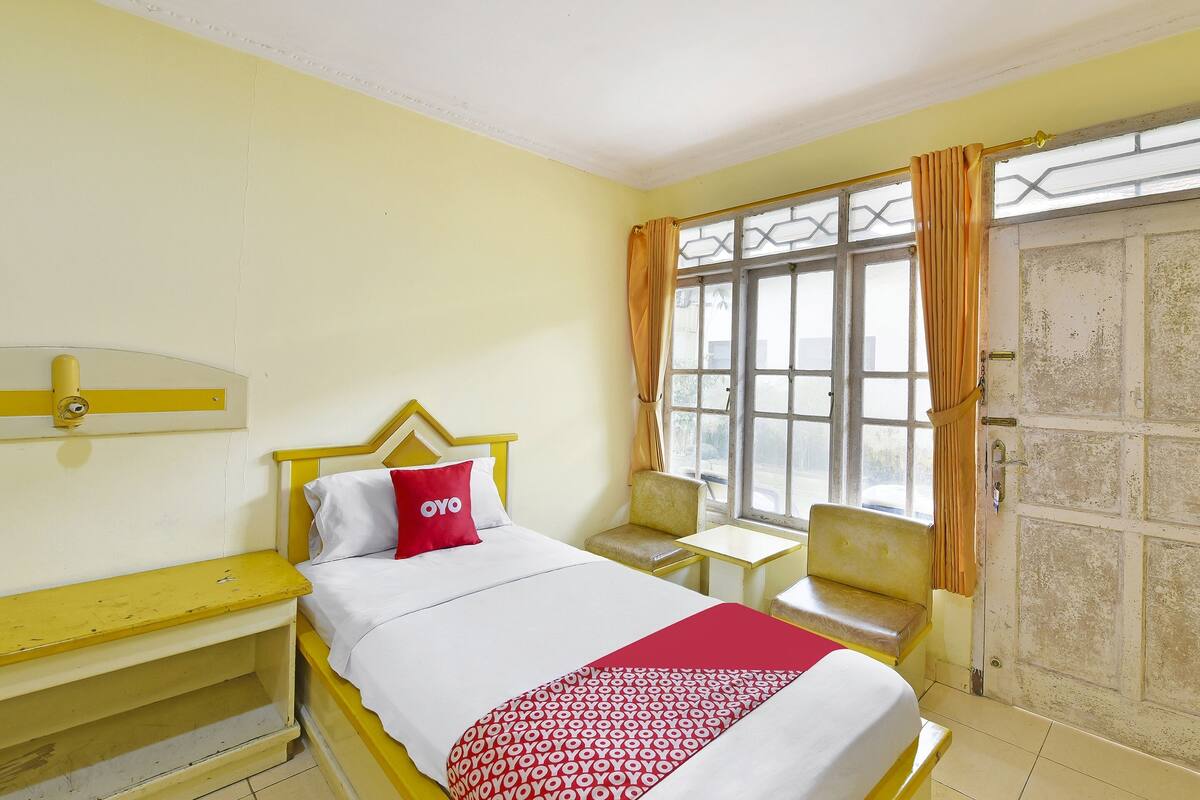Une chambre d’hôtel avec un lit, une petite table, une chaise et une fenêtre avec des rideaux.