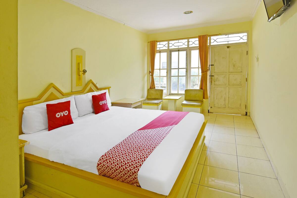 Une chambre d’hôtel avec un lit, un bureau, une chaise et une fenêtre avec des rideaux.