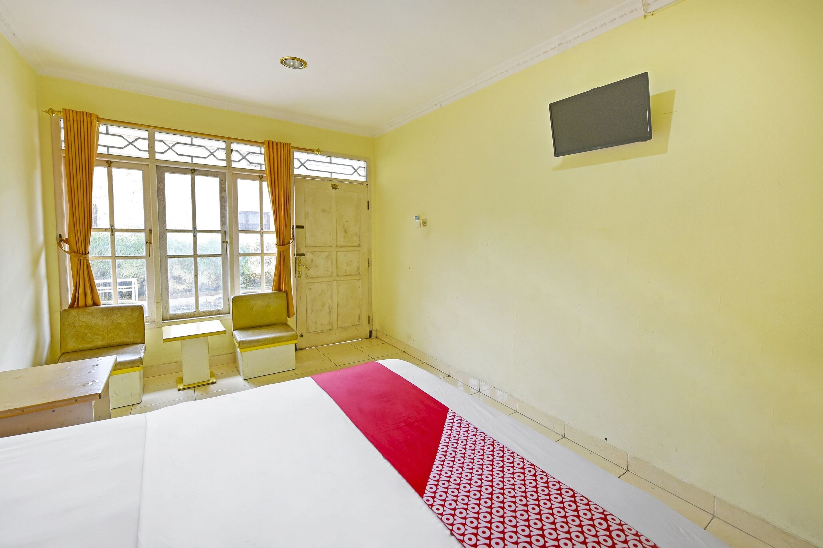Habitación de hotel con una cama, una mesita, dos sillas, un ventanal con cortinas y un televisor en la pared.
