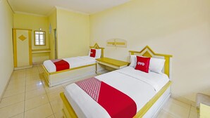 Een hotelkamer met twee bedden, elk met een rode en witte dekbedovertrek, en een kleine tafel ertussen.