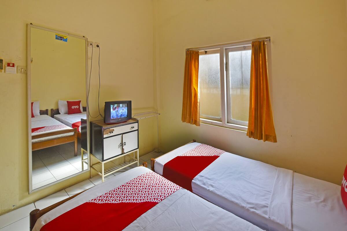 Une chambre d’hôtel avec deux lits simples, un téléviseur posé sur une petite table, un miroir et une fenêtre avec des rideaux.