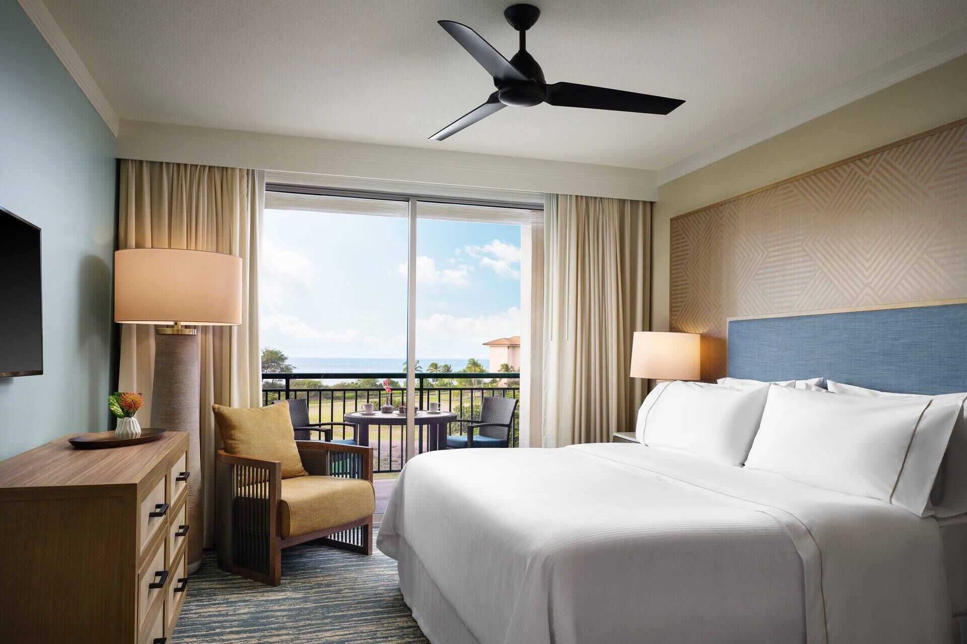 Ein Hotelzimmer mit Bett, Stuhl, Schreibtisch, Lampe und Deckenventilator.