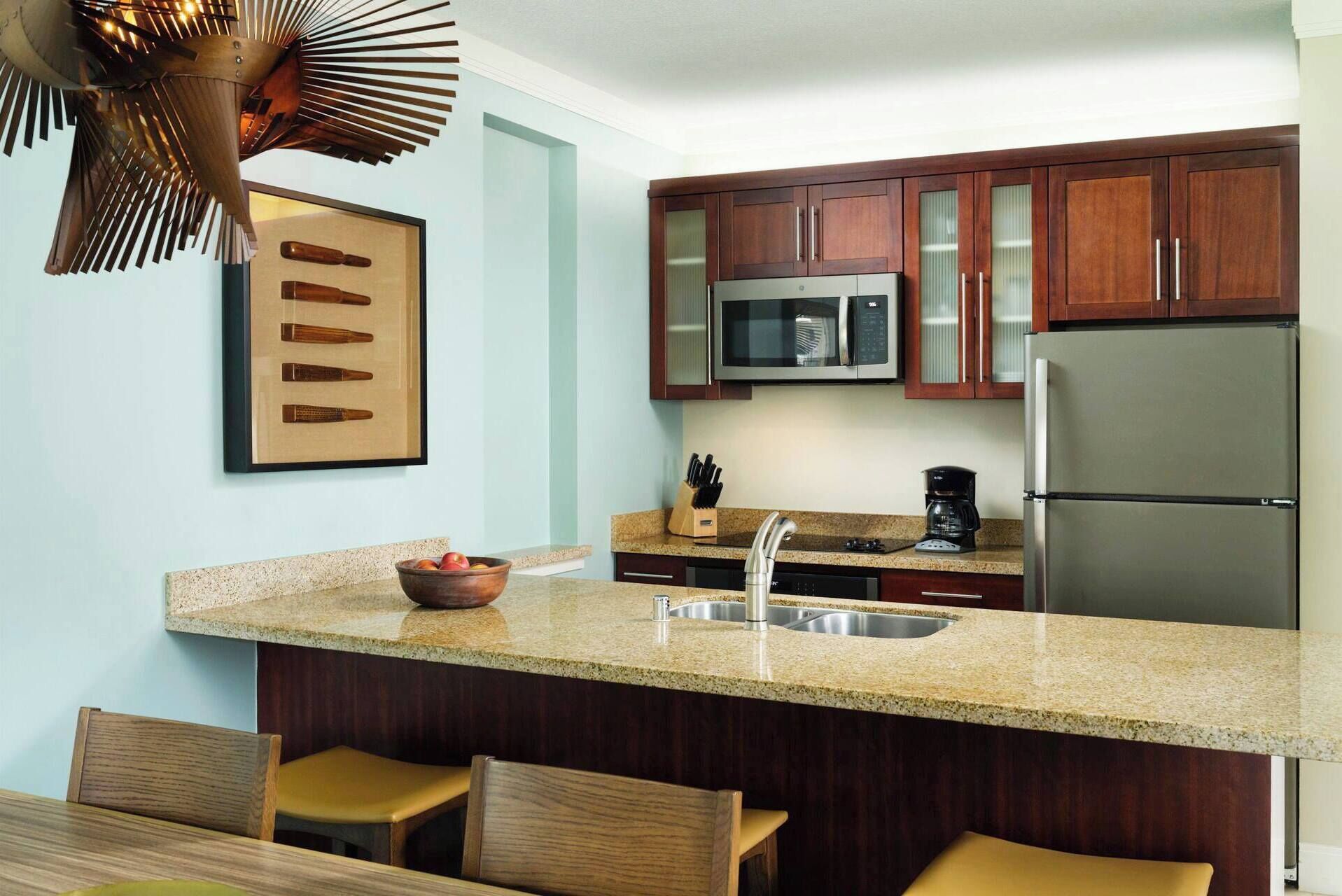 A modern kitchen with wooden cabinets, a stainless steel refrigerator, a microwave, and a granite countertop.
