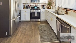 Una cocina moderna con armarios blancos, electrodomésticos de acero inoxidable, suelo de madera y una ventana con cortina.