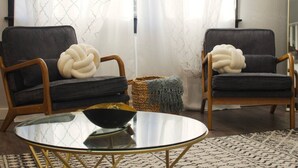 Una sala de estar con dos sillones grises oscuros, una mesa de centro redonda de vidrio y una cesta tejida.