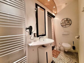 A bathroom with a white sink, a mirror, a toilet, and a shower area.