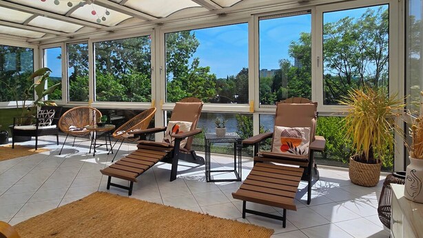 Une véranda avec de grandes fenêtres, un sol carrelé et plusieurs fauteuils confortables.