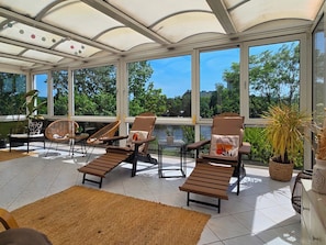 A sunroom with large windows, a tiled floor, and several lounge chairs.